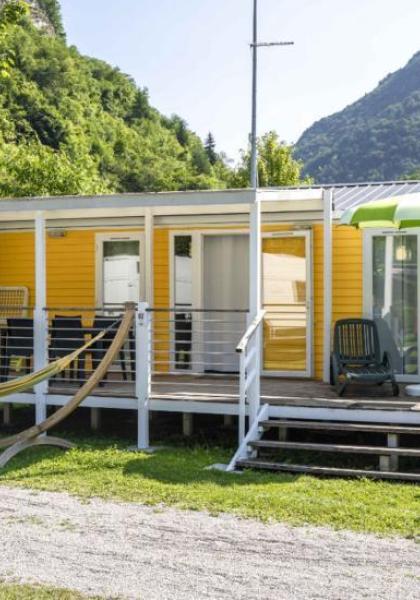 Geel huis met veranda, ligstoelen en hangmat, omringd door groene bergen.